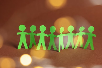 Photo of Paper figures of people holding hands on brown background, bokeh effect