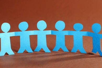 Photo of Paper figures of people holding hands on brown background, closeup