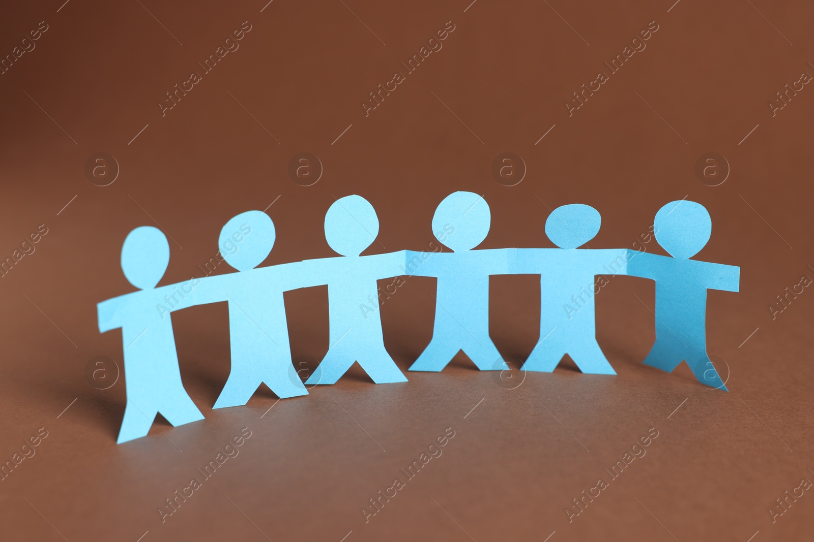 Paper figures of people holding hands on brown background Photo of Paper figures of people holding hands on brown background