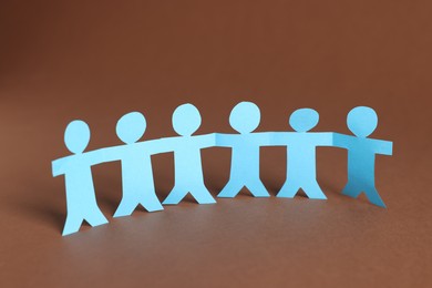 Photo of Paper figures of people holding hands on brown background