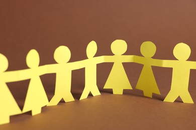 Photo of Paper figures of people holding hands on brown background, closeup
