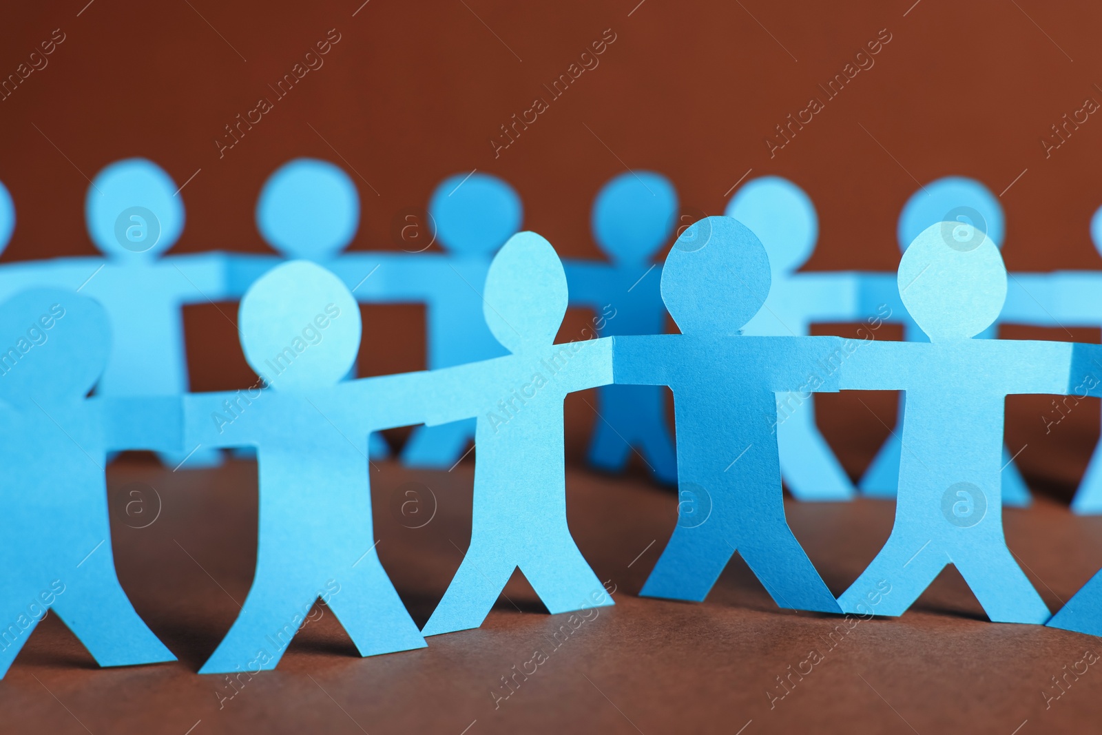 Paper figures of people holding hands on brown background, closeup Photo of Paper figures of people holding hands on brown background, closeup