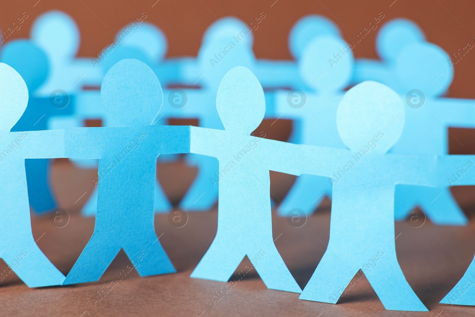 Paper figures of people holding hands on brown background, closeup Photo of Paper figures of people holding hands on brown background, closeup