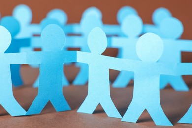 Photo of Paper figures of people holding hands on brown background, closeup