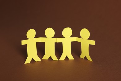 Photo of Paper figures of people holding hands on brown background, closeup