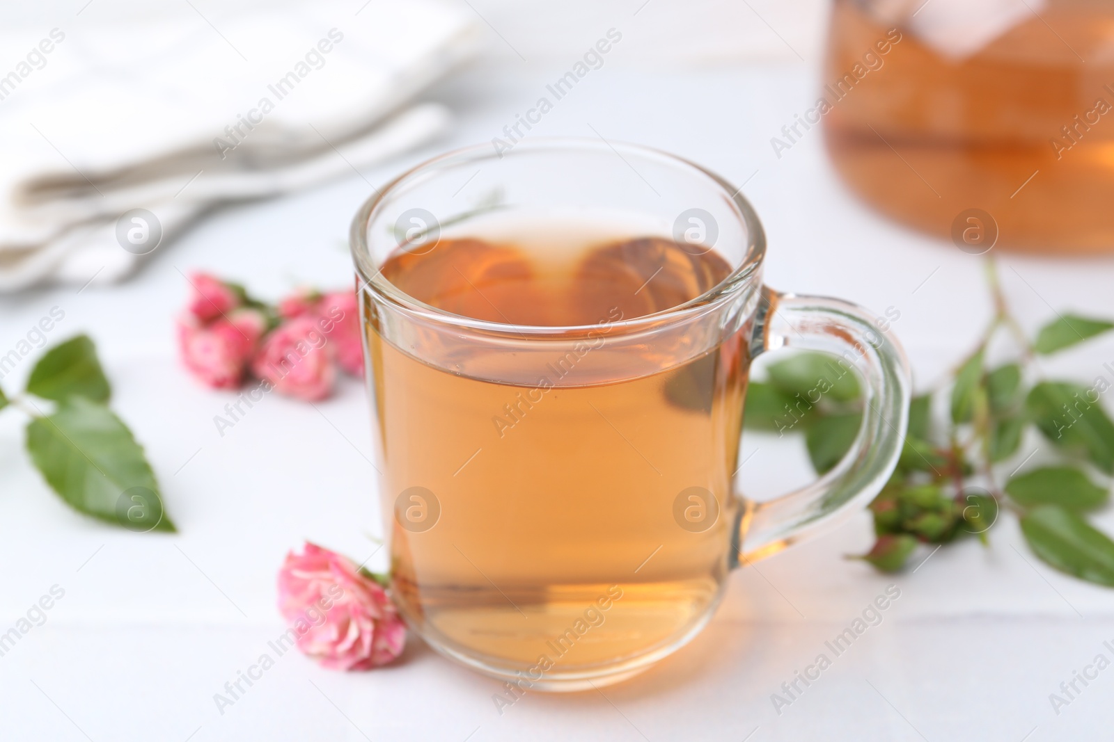 Aromatic tea in glass cup, roses and green leaves on white table, closeup Photo of Aromatic tea in glass cup, roses and green leaves on white table, closeup