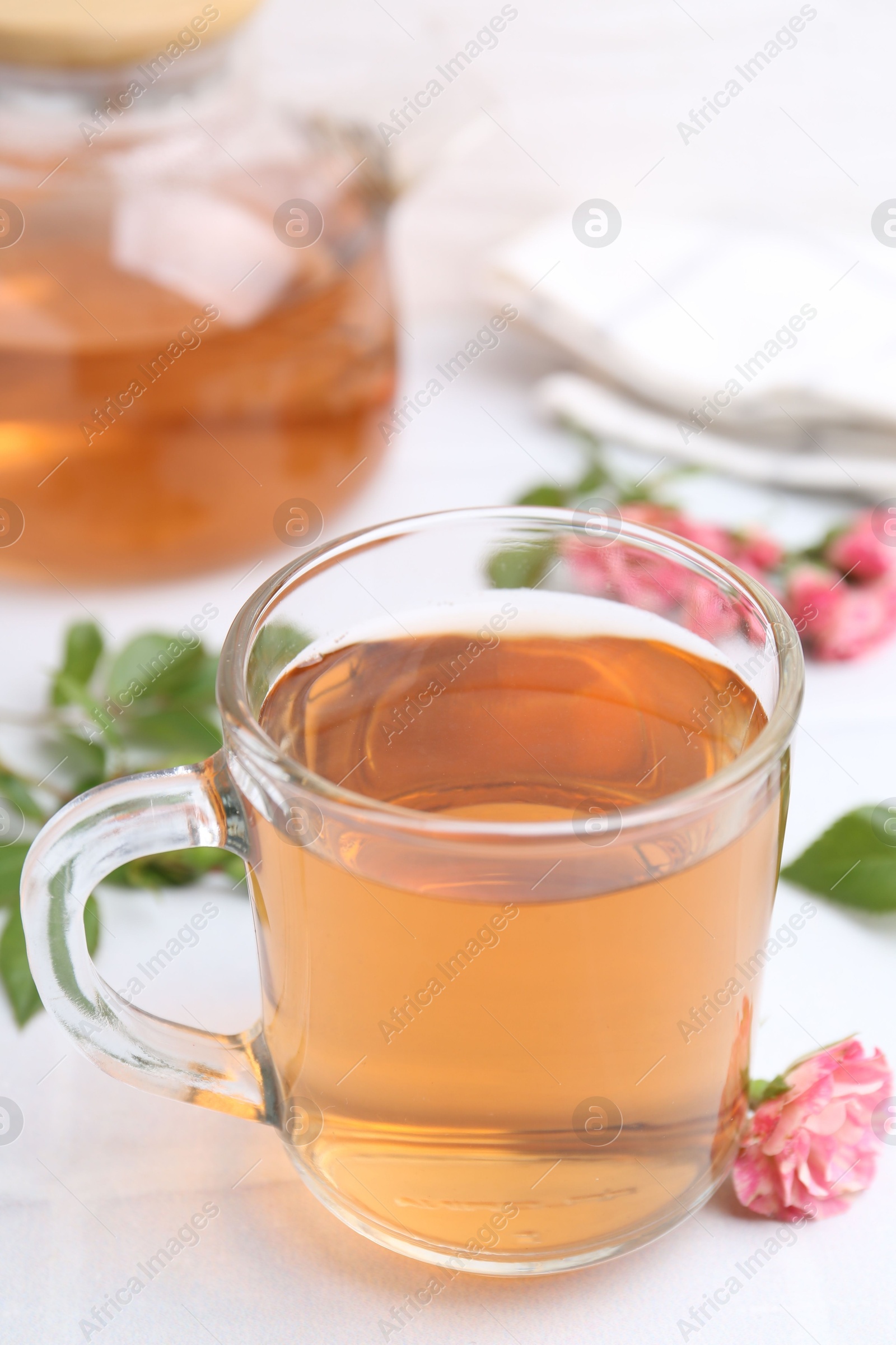 Aromatic tea in glass cup, roses and green leaves on white table, closeup Photo of Aromatic tea in glass cup, roses and green leaves on white table, closeup