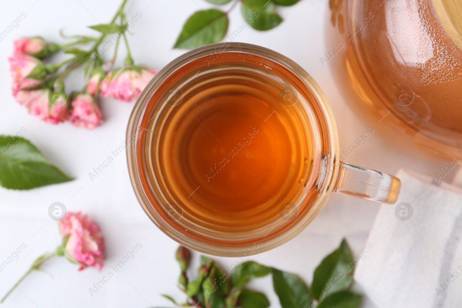 Aromatic tea in glass cup, roses and green leaves on white table, flat lay Photo of Aromatic tea in glass cup, roses and green leaves on white table, flat lay