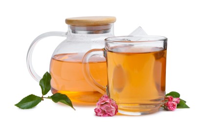 Photo of Aromatic tea in glass cup, teapot, roses and green leaves isolated on white