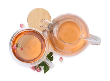 Photo of Aromatic tea in glass cup, teapot, roses and green leaves isolated on white, top view