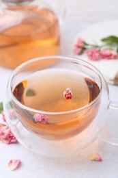 Photo of Aromatic tea in glass cup, teapot and roses on light table, closeup