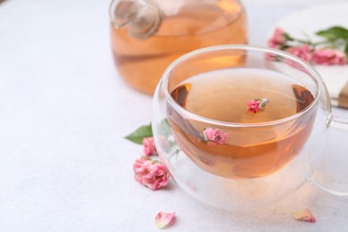 Photo of Aromatic tea in glass cup, teapot and roses on light table, closeup. Space for text