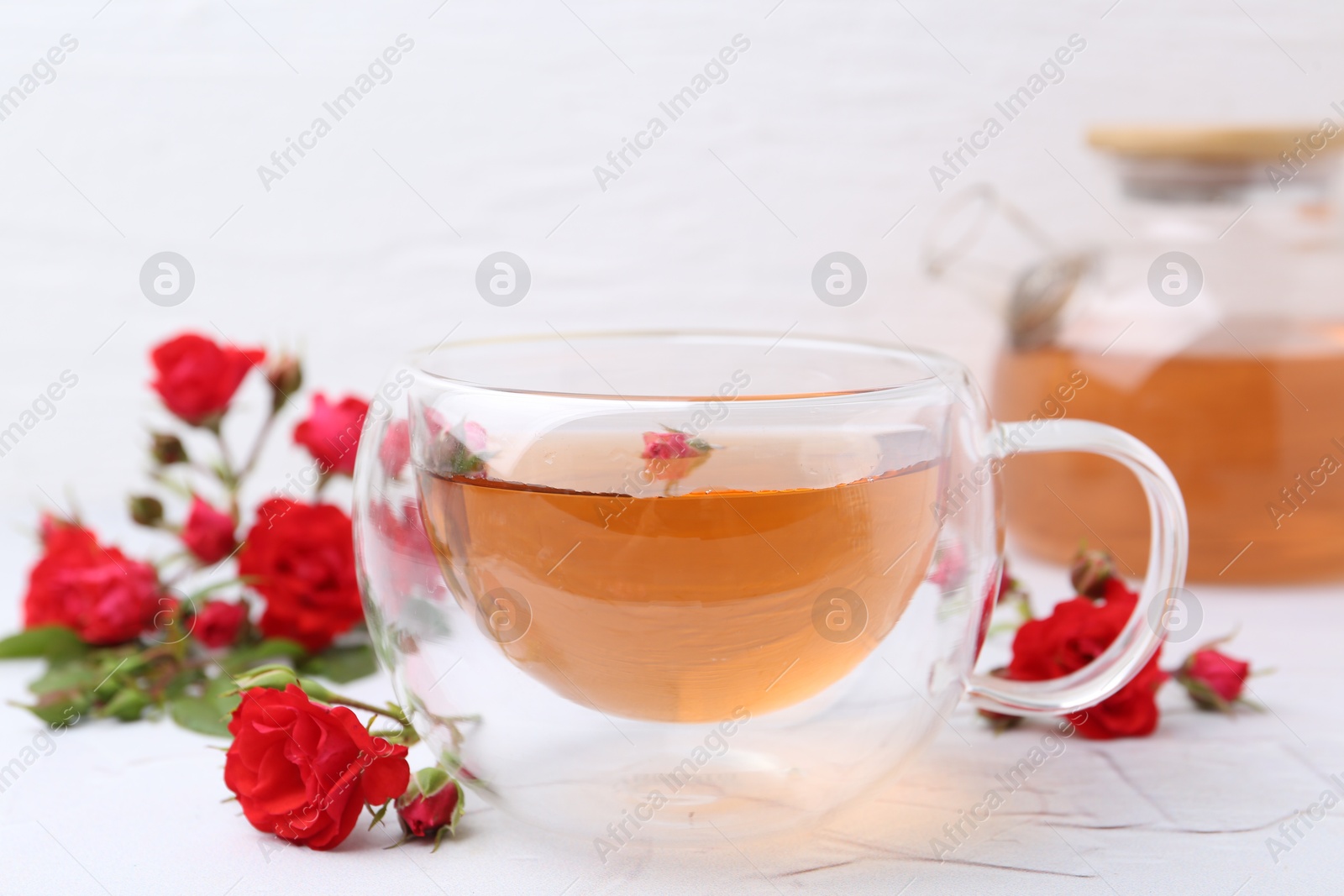 Aromatic tea in glass cup, roses and green leaves on white table, closeup Photo of Aromatic tea in glass cup, roses and green leaves on white table, closeup