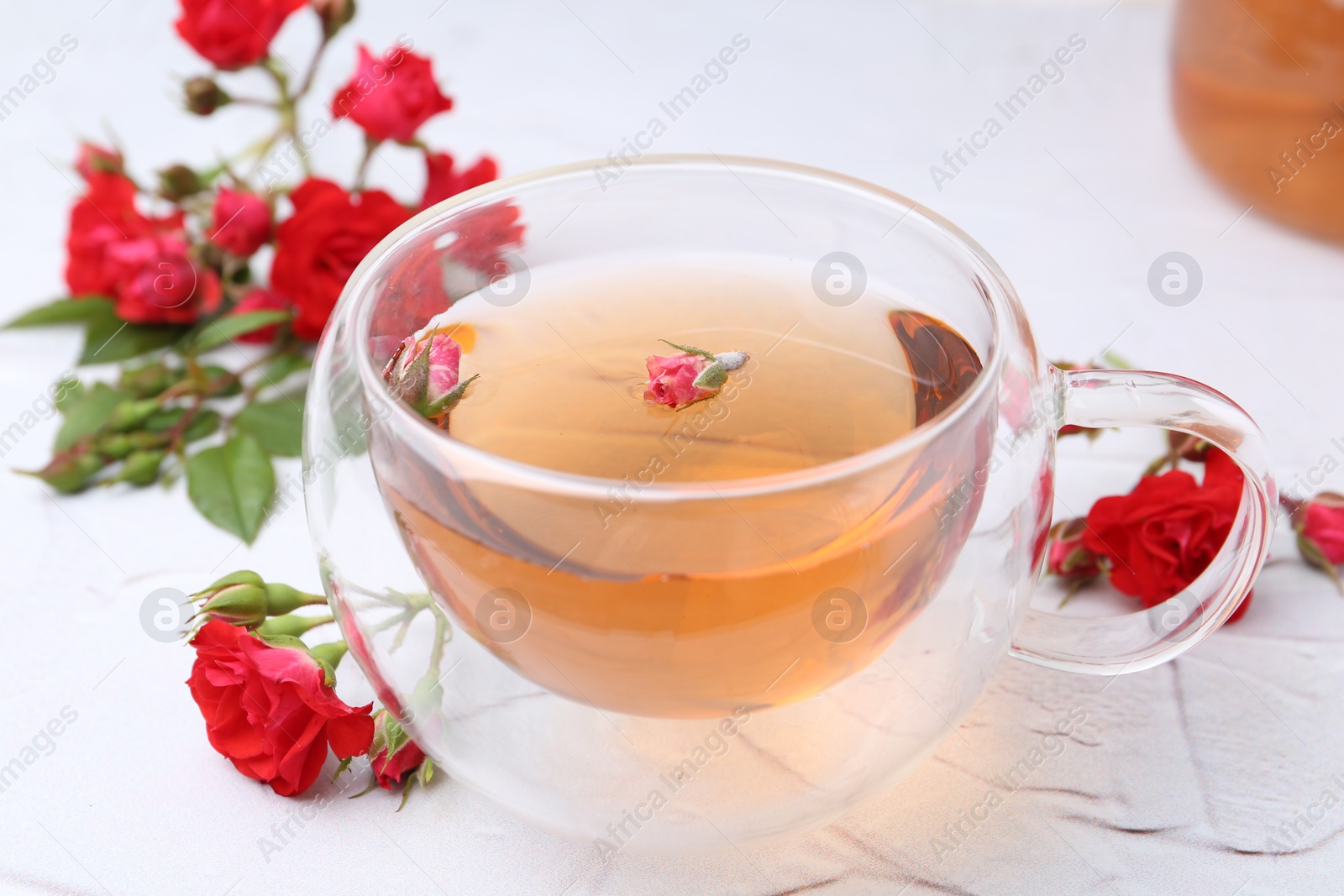 Aromatic tea in glass cup, roses and green leaves on white table, closeup Photo of Aromatic tea in glass cup, roses and green leaves on white table, closeup