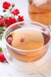 Photo of Aromatic tea in glass cup and roses on white table, closeup