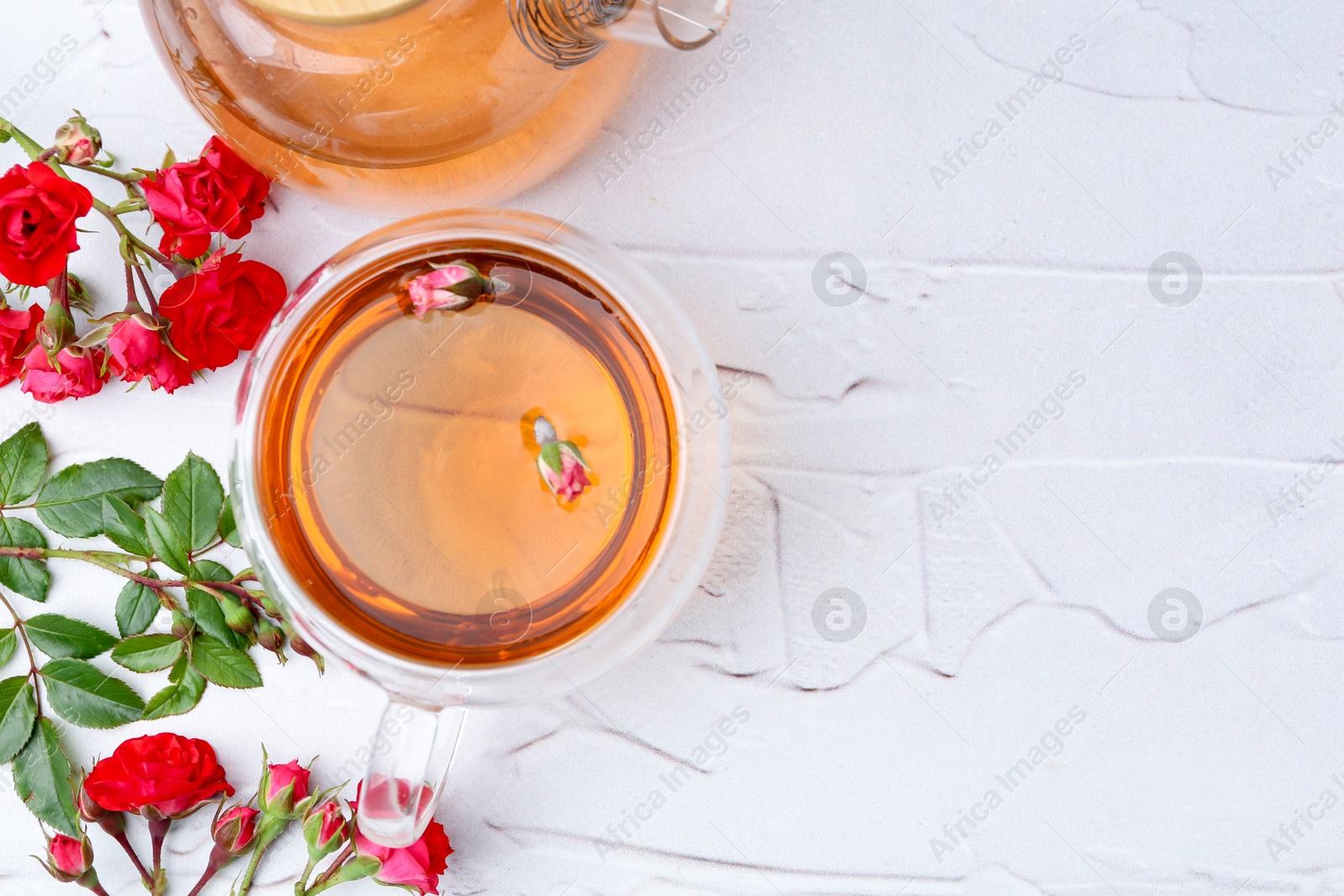 Aromatic tea in glass cup, teapot, roses and green leaves on white table, flat lay. Space for text Photo of Aromatic tea in glass cup, teapot, roses and green leaves on white table, flat lay. Space for text