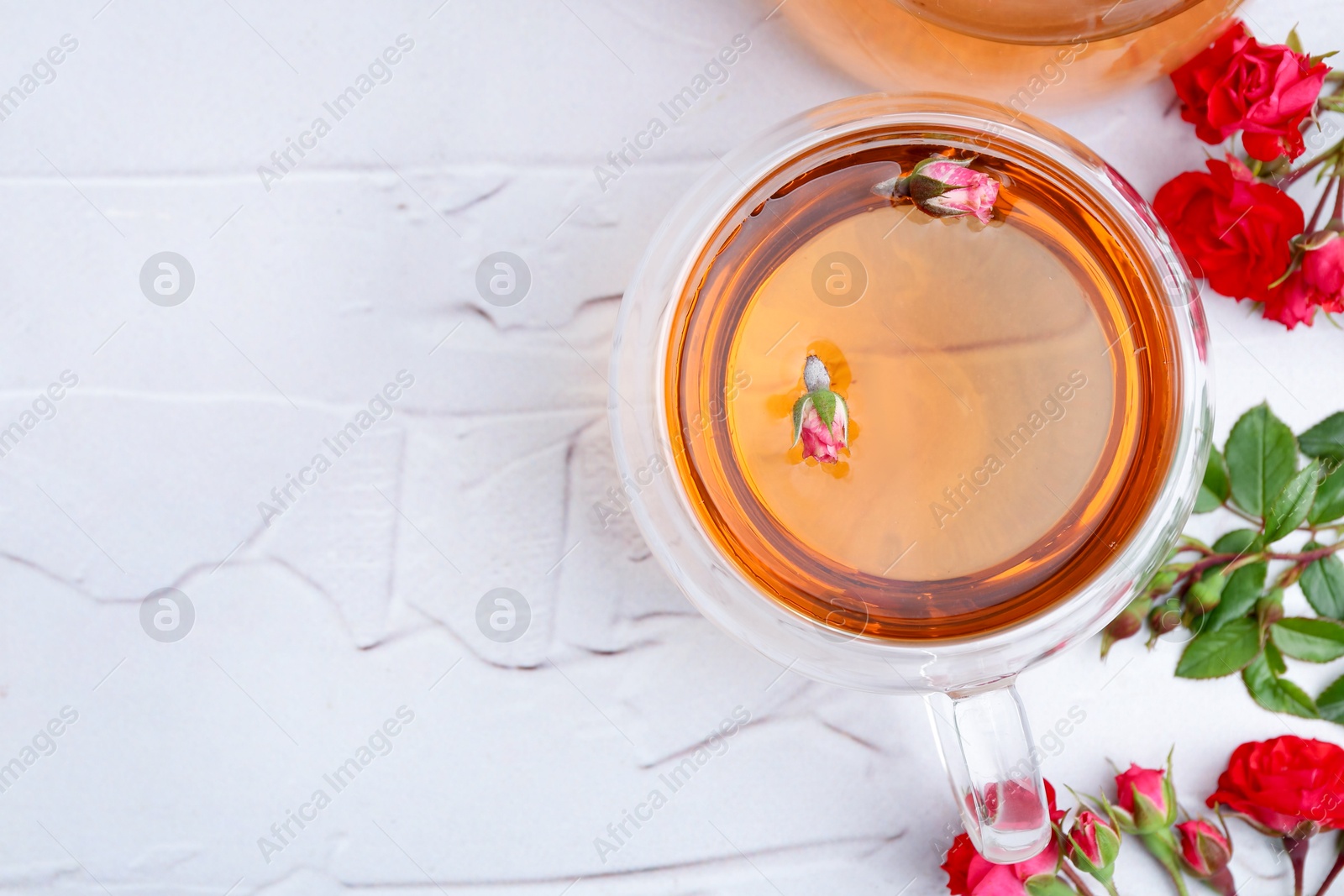 Aromatic tea in glass cup, roses and green leaves on white table, flat lay. Space for text Photo of Aromatic tea in glass cup, roses and green leaves on white table, flat lay. Space for text