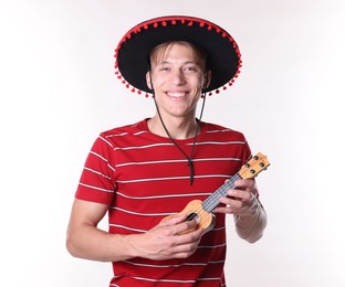 Photo of Smiling man in black Flamenco hat playing ukulele on white background