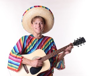 Photo of Smiling man in sombrero hat and colorful poncho playing guitar on white background