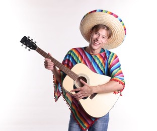 Photo of Smiling man in sombrero hat and colorful poncho playing guitar on white background