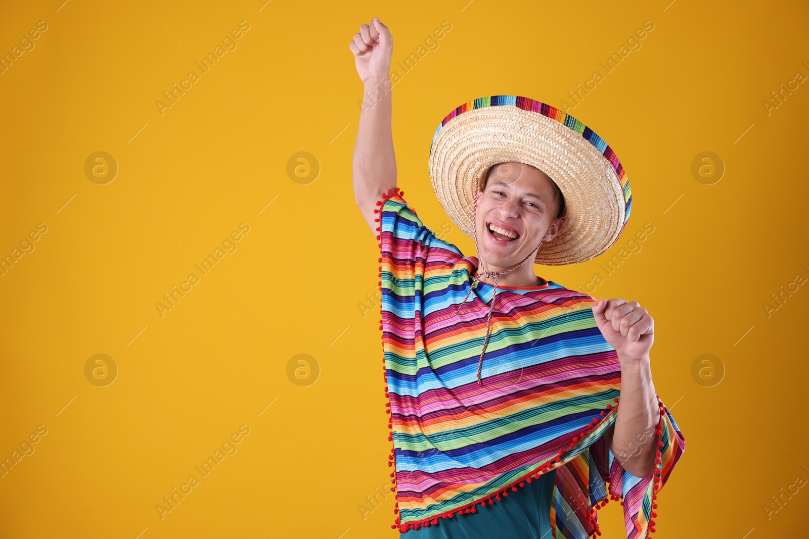 Photo of Happy man in sombrero hat and colorful poncho dancing on yellow background. Space for text