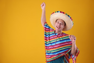 Photo of Happy man in sombrero hat and colorful poncho dancing on yellow background. Space for text