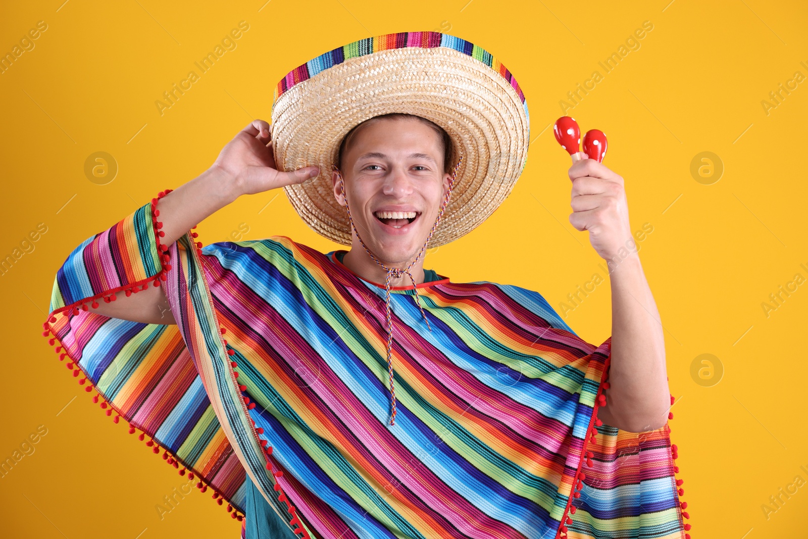Photo of Happy man in sombrero hat, colorful poncho and maracas on yellow background