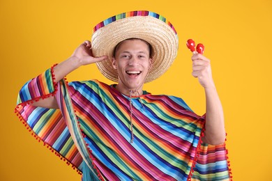 Photo of Happy man in sombrero hat, colorful poncho and maracas on yellow background