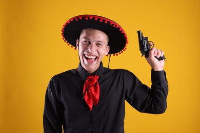 Photo of Happy man in black Flamenco hat with gun on yellow background