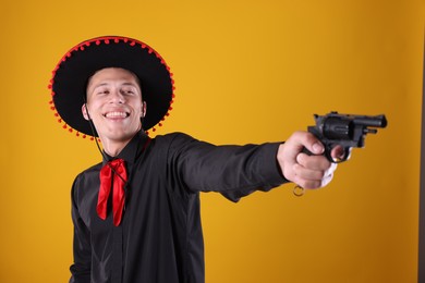 Photo of Happy man in black Flamenco hat with gun on yellow background