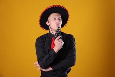 Photo of Man in black Flamenco hat with gun on yellow background