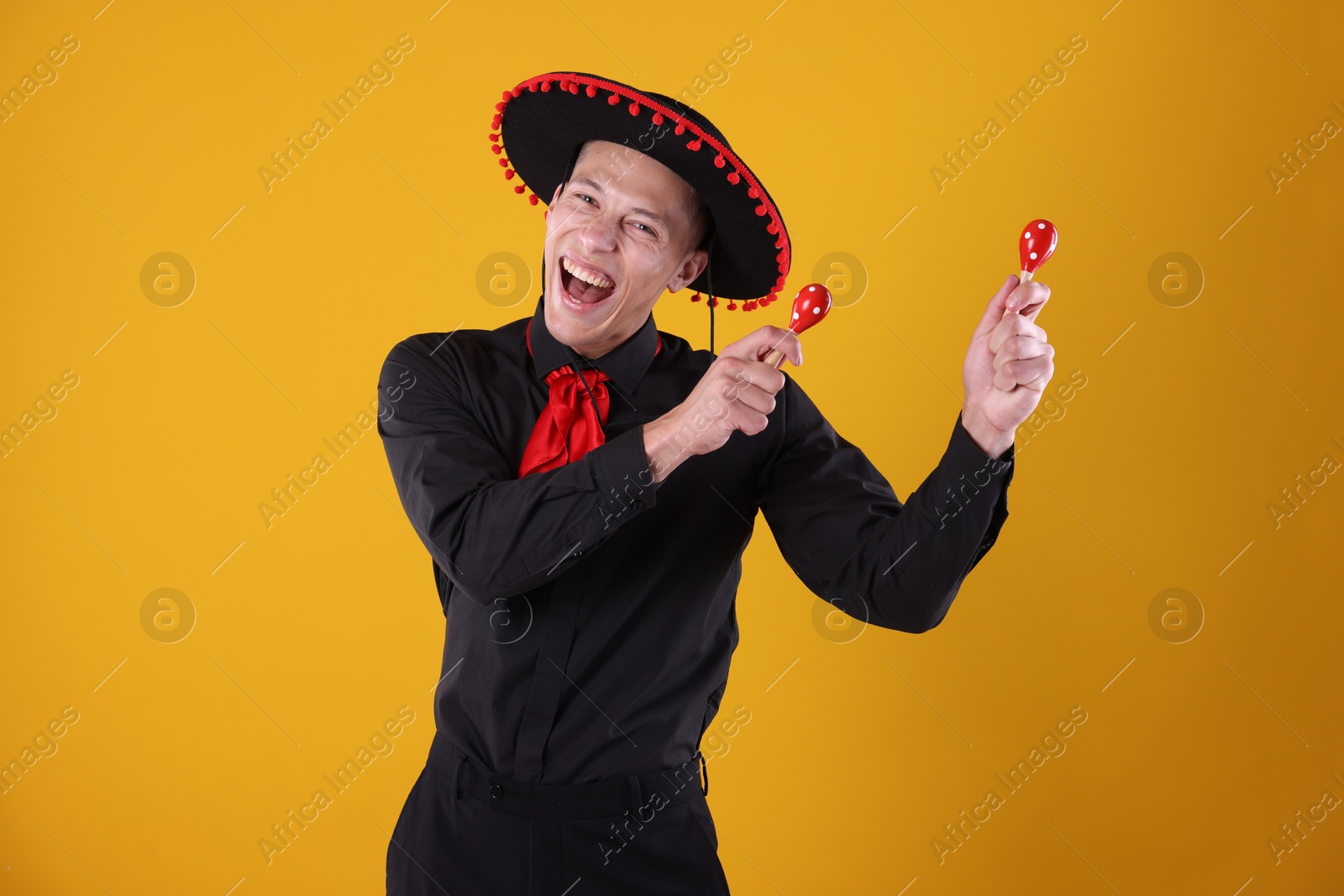 Photo of Portrait of happy man in black Flamenco hat playing maracas on yellow background