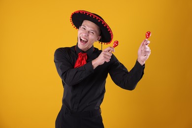 Photo of Portrait of happy man in black Flamenco hat playing maracas on yellow background