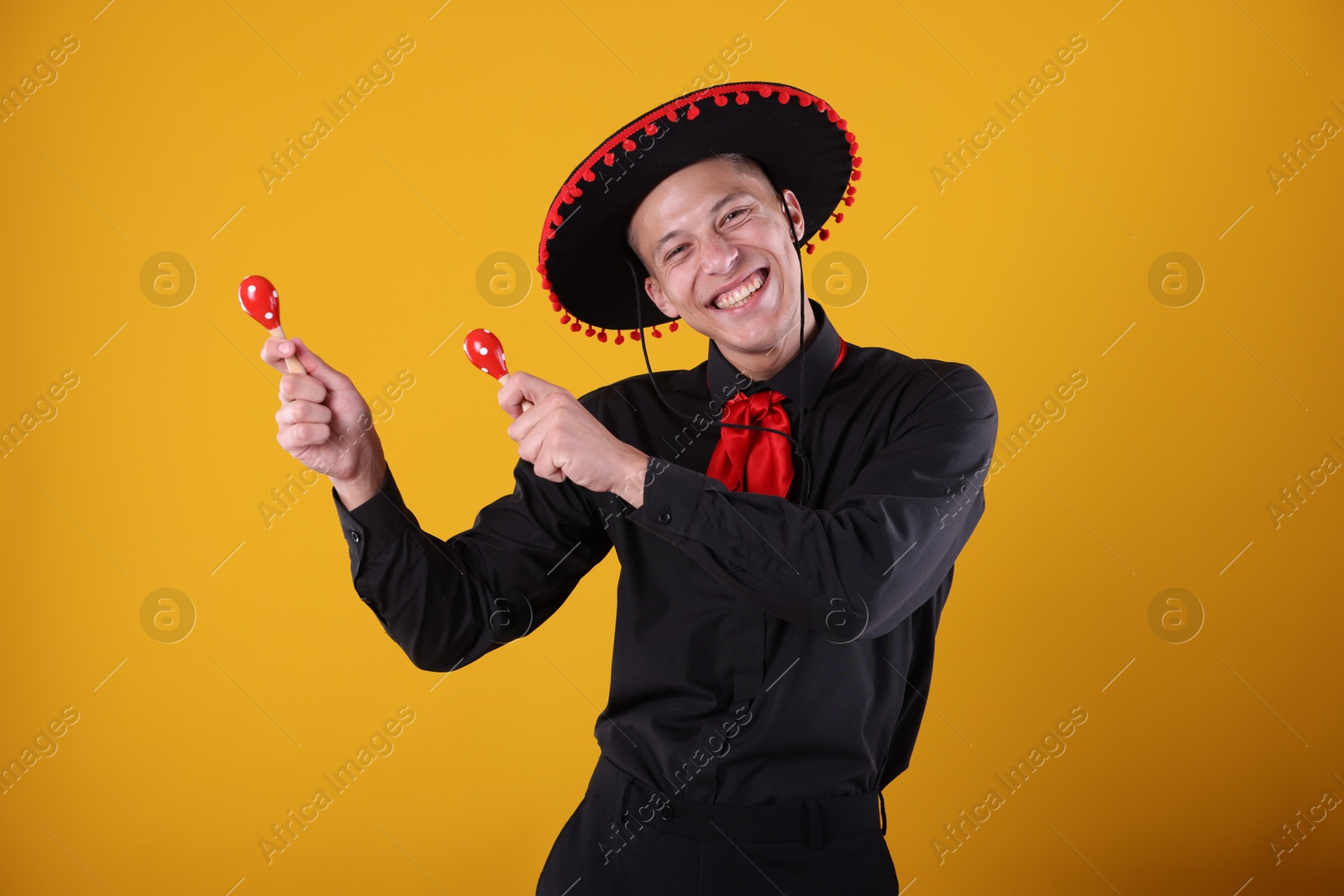 Photo of Portrait of happy man in black Flamenco hat playing maracas on yellow background