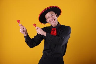 Photo of Portrait of happy man in black Flamenco hat playing maracas on yellow background
