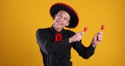 Photo of Portrait of happy man in black Flamenco hat playing maracas on yellow background