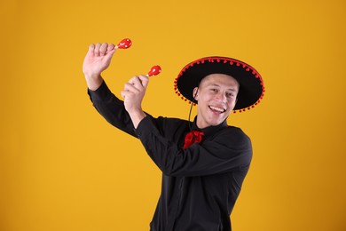 Photo of Portrait of happy man in black Flamenco hat playing maracas on yellow background