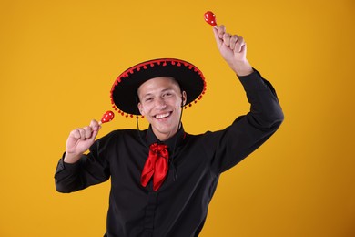 Photo of Portrait of happy man in black Flamenco hat playing maracas on yellow background