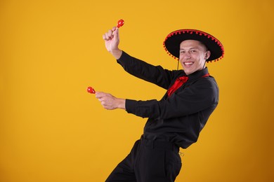 Photo of Portrait of happy man in black Flamenco hat playing maracas on yellow background