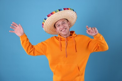 Photo of Happy man in sombrero hat dancing on light blue background