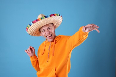 Photo of Happy man in sombrero hat dancing on light blue background