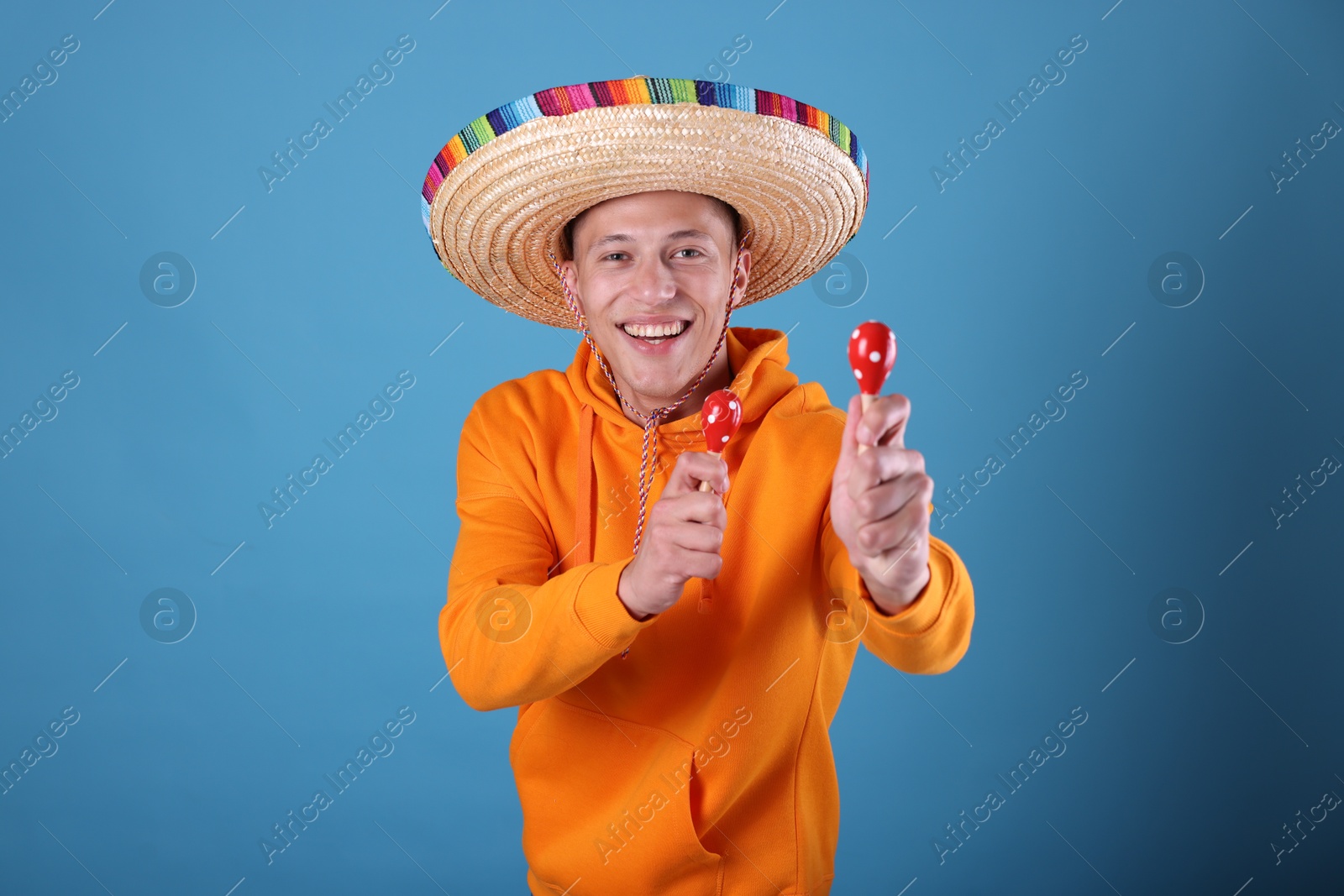 Photo of Happy man in sombrero hat playing maracas on light blue background