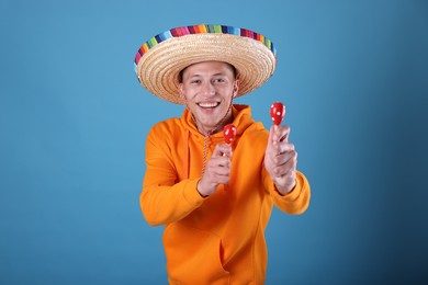 Photo of Happy man in sombrero hat playing maracas on light blue background