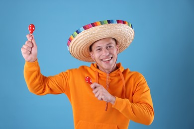 Photo of Happy man in sombrero hat playing maracas on light blue background
