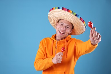 Photo of Happy man in sombrero hat playing maracas on light blue background