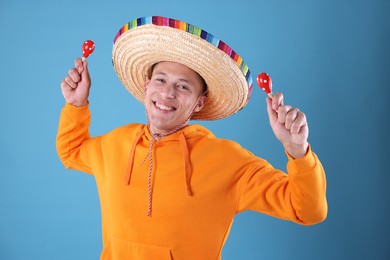 Photo of Happy man in sombrero hat playing maracas on light blue background