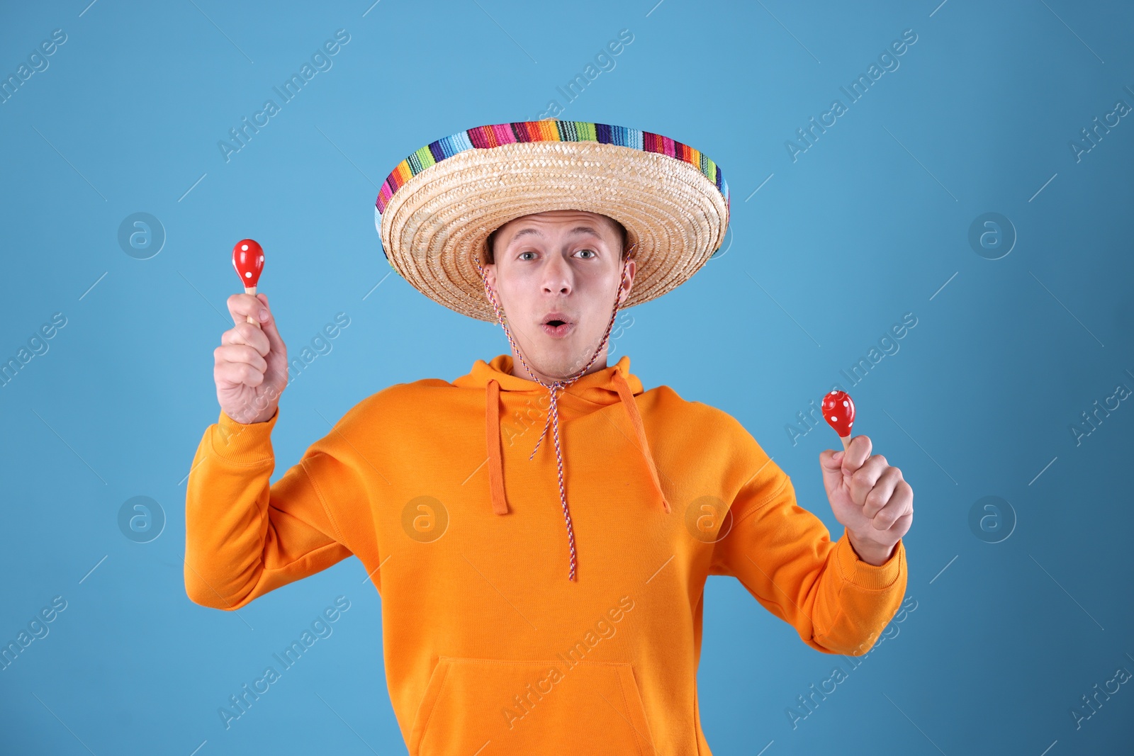 Photo of Emotional man in sombrero hat playing maracas on light blue background