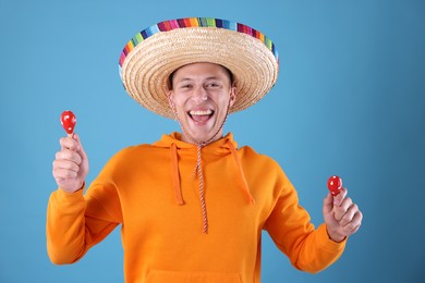 Photo of Happy man in sombrero hat playing maracas on light blue background