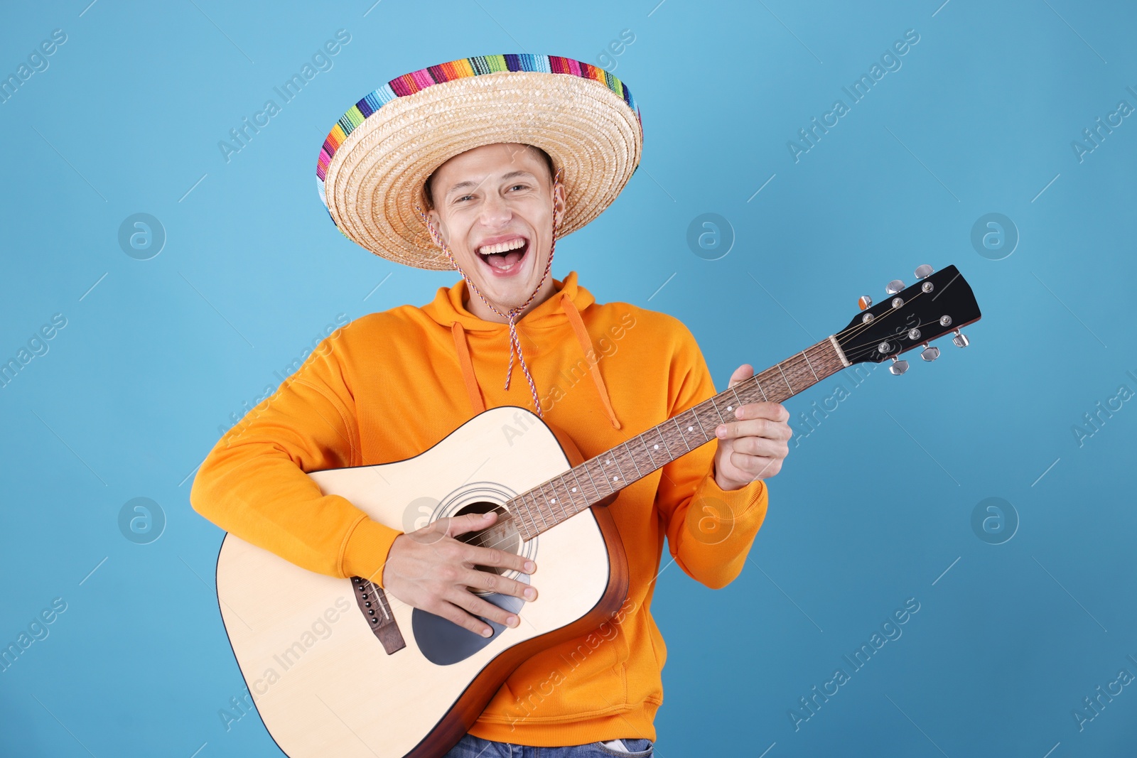 Photo of Happy man in sombrero hat playing guitar on light blue background