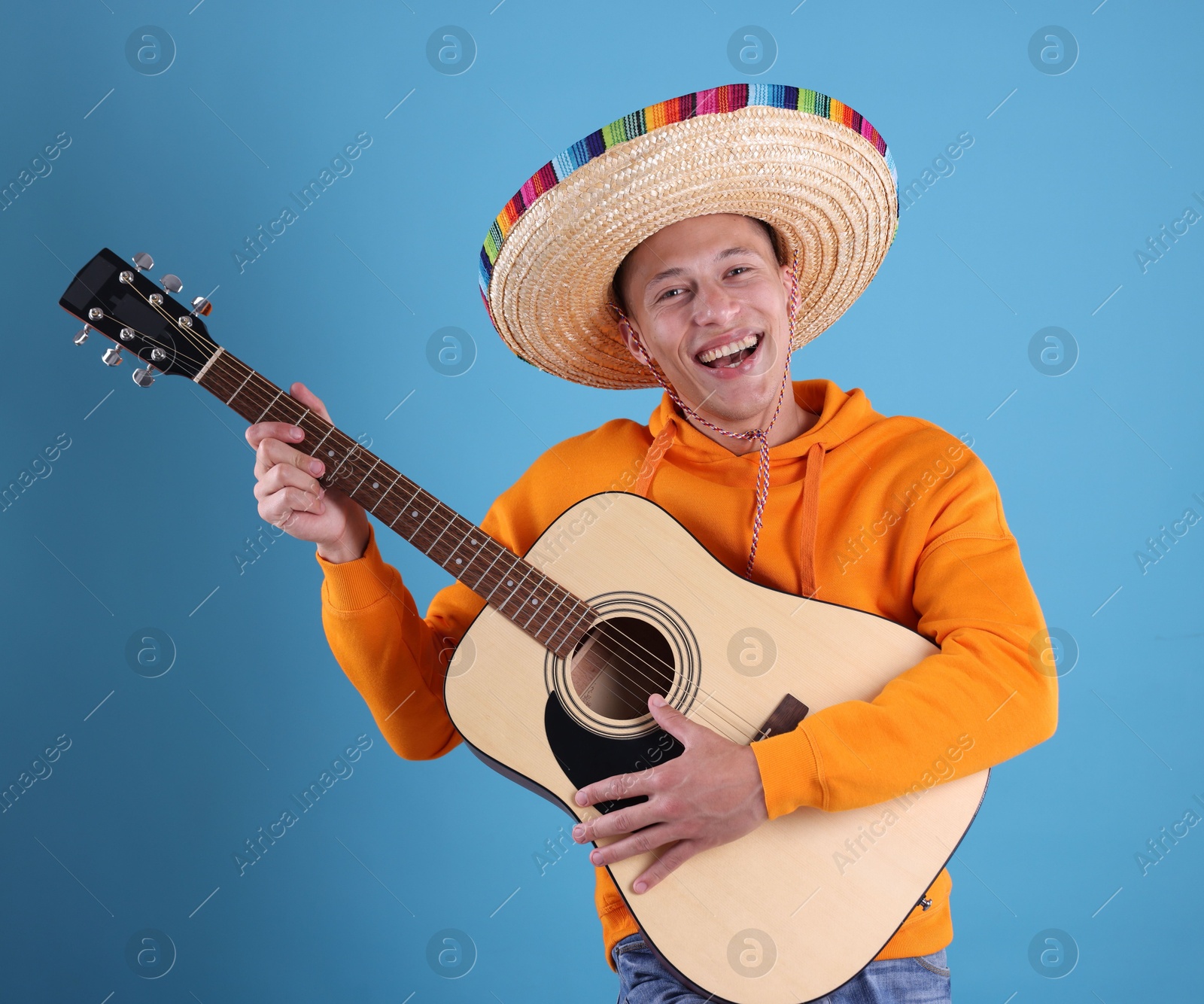 Photo of Happy man in sombrero hat playing guitar on light blue background